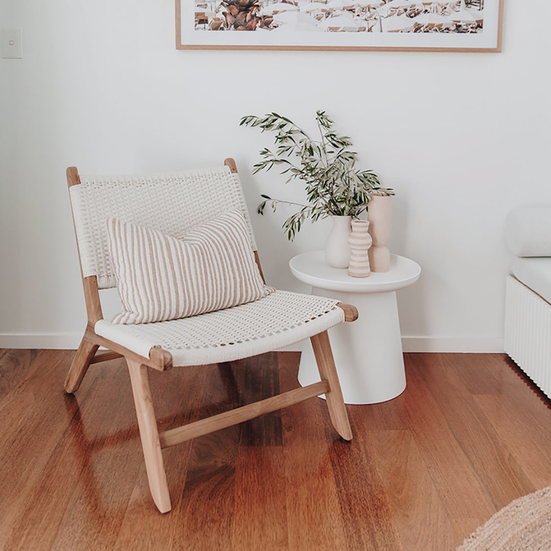 Single Zen Lazy Chair - White - Open Weave placed beside a modern white side table with sculptural vases and a leafy branch. The chair features a handwoven open-grid seat in crisp white with a natural teak wood frame, styled with a striped lumbar cushion for added comfort and visual interest.