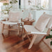 Pair of Zen Lazy Chairs - White - Open Weave styled indoors with blush-toned patterned cushions, flanking a round teak side table decorated with minimalist ceramic vases. The white woven seats and backs contrast with the warm teak frames and hardwood flooring, creating a coastal-boho lounge vignette.