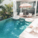 Poolside scene with two Zen Lazy Chairs - White - Open Weave arranged under a thatched umbrella, accompanied by a small teak table and striped cushions. The relaxed outdoor setting includes white pool floats and tropical greenery, highlighting the chair’s suitability for modern resort-inspired patios.