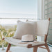 Close-up of Zen Lazy Chair on a balcony with a serene landscape view, featuring a soft beige throw pillow and a white summer hat resting on the seat. The white open weave and teak wood structure evoke a tranquil, resort-style outdoor escape.