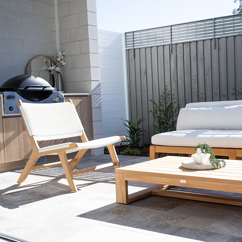 Lifestyle image of Zen Lazy Chair – White – Close Weave styled on a modern patio with teak coffee table and white outdoor sofa.