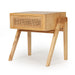Angled view of the Castaway Bedside Table with natural timber frame, rattan drawer and tapered legs