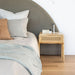 Castaway Bedside Table styled beside an upholstered bed in a soft neutral bedroom