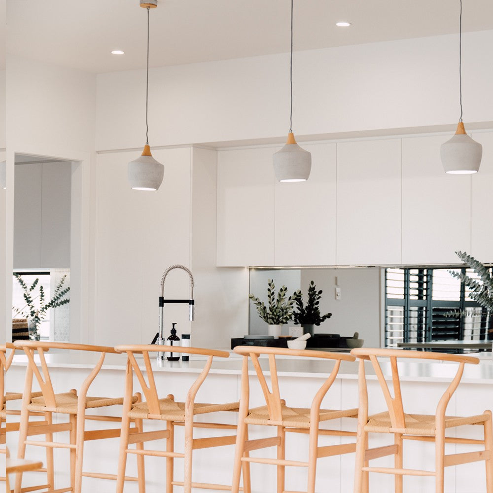 Wishbone Counter Stool in Natural Oak close up of multiple stools at a white kitchen bench with pendant lights overhead.