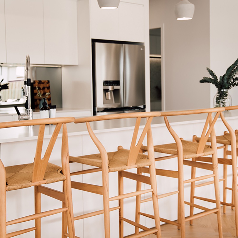 Wishbone Counter Stool in Natural Oak row of stools at a white kitchen bench with stainless steel fridge and modern kitchen styling.
