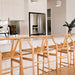 Wishbone Counter Stool in Natural Oak row of stools at a white kitchen bench with stainless steel fridge and modern kitchen styling.