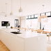 Wishbone Counter Stool in Natural Oak shown in a bright kitchen and dining space with white island bench, pendant lights and timber dining furniture.