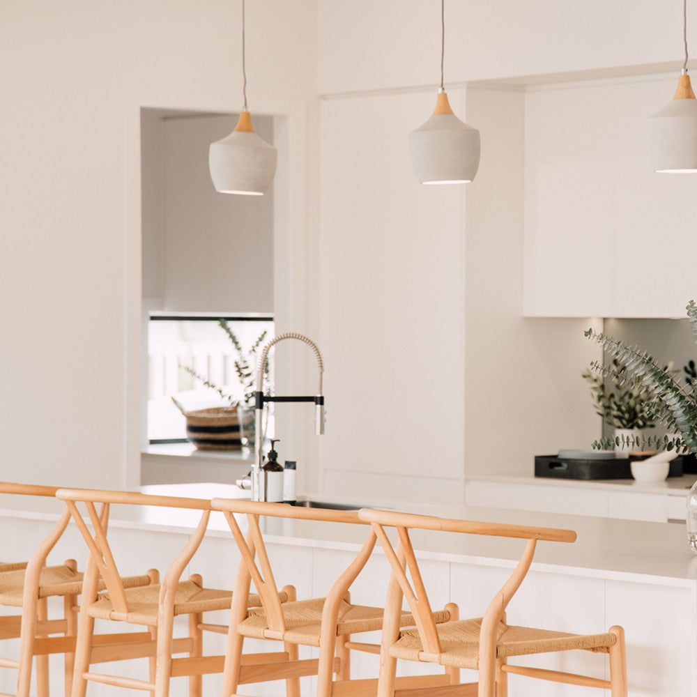 Wishbone Counter Stool in Natural Oak shown at a white kitchen bench with pendant lights, black tapware and soft neutral styling.