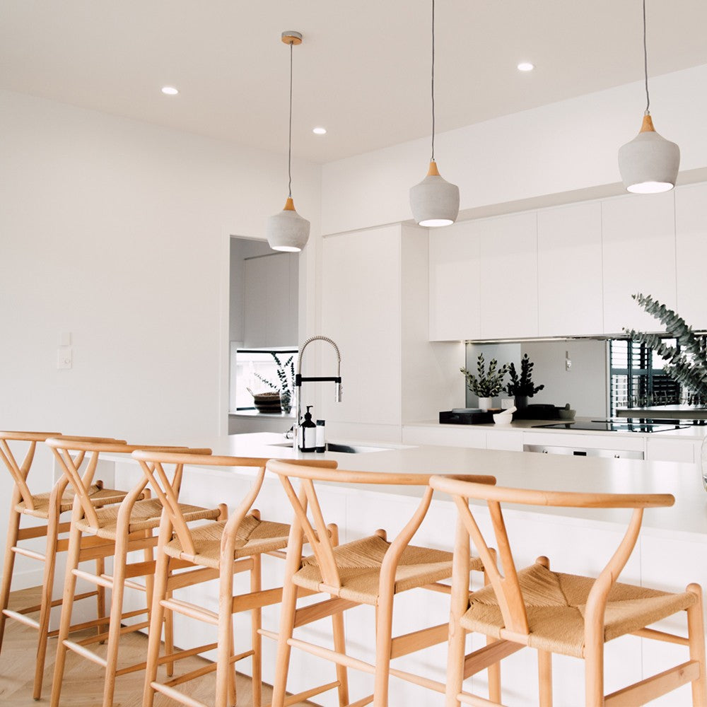Wishbone Counter Stool in Natural Oak styled beneath pendant lights at a white kitchen island with a modern coastal interior.