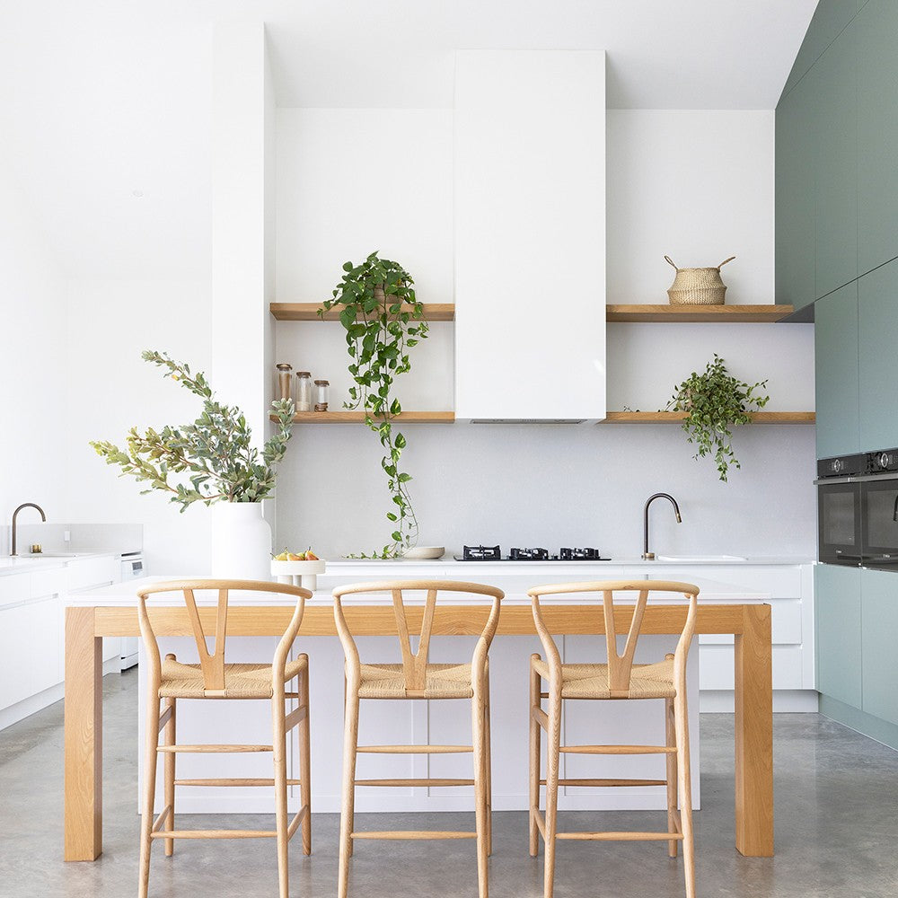 Wishbone Counter Stool in Natural Oak styled at a modern white kitchen island with woven cord seats, timber legs and light coastal interiors.