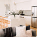 Wishbone Counter Stool in Natural Oak in an open plan kitchen and living room with white island bench, grey sofa and coastal home styling.