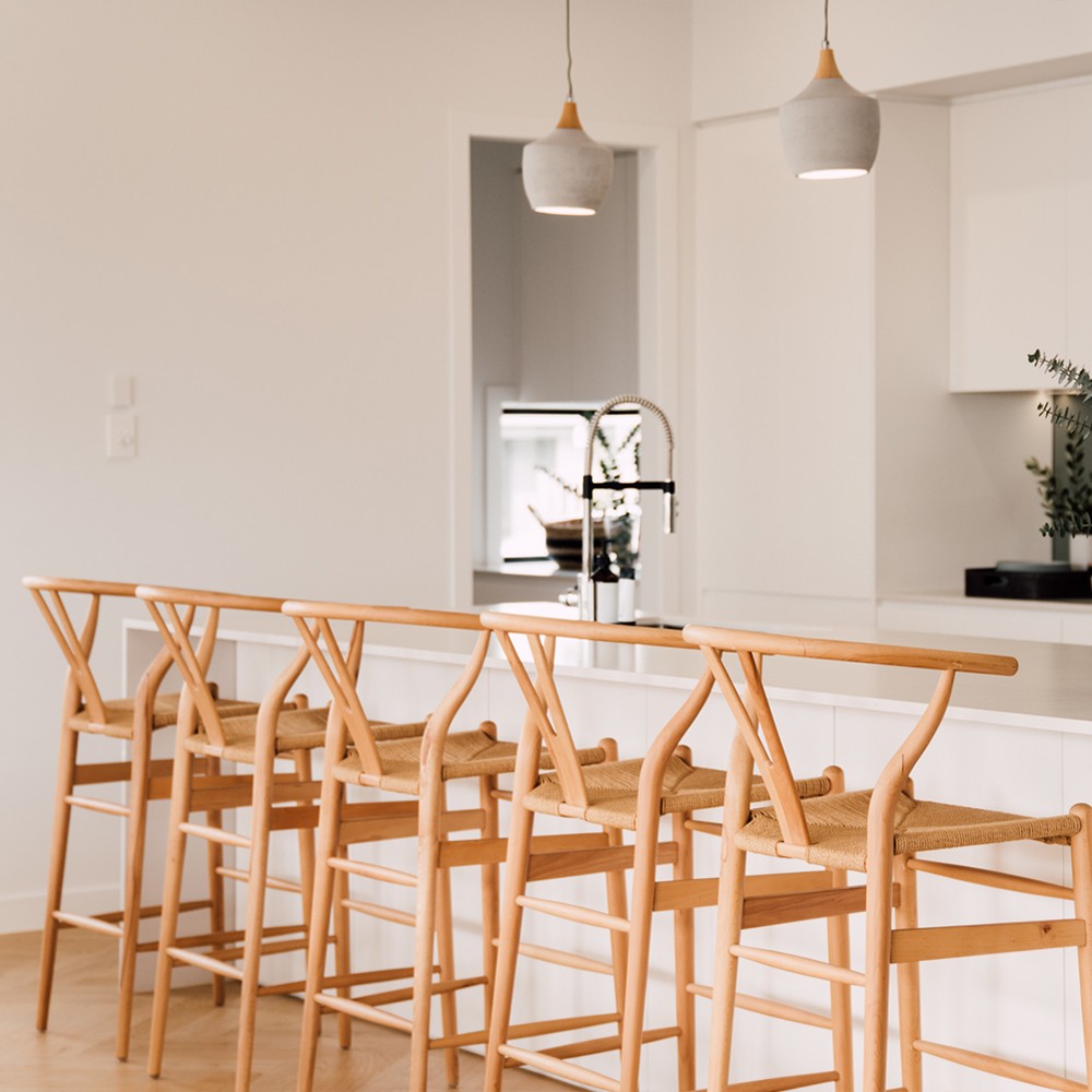 Wishbone Counter Stool in Natural Oak row of stools styled at a white kitchen island with soft pendant lights and warm timber flooring.
