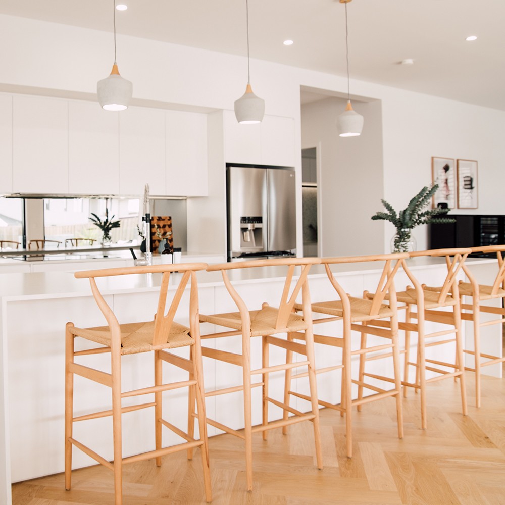 Wishbone Counter Stool in Natural Oak set of five styled along a white kitchen bench with timber floors and pendant lighting.