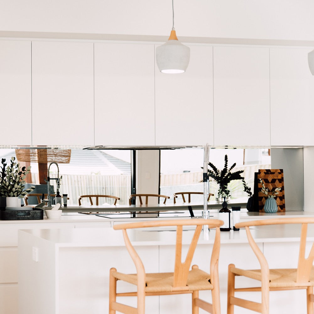 Wishbone Counter Stool in Natural Oak at a white kitchen island with mirrored splashback, pendant light and natural timber accents.