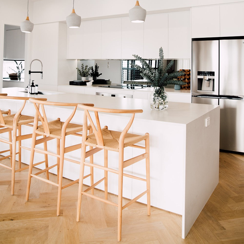 Wishbone Counter Stool in Natural Oak set of three styled at a white kitchen island with eucalyptus branches and stainless steel fridge.